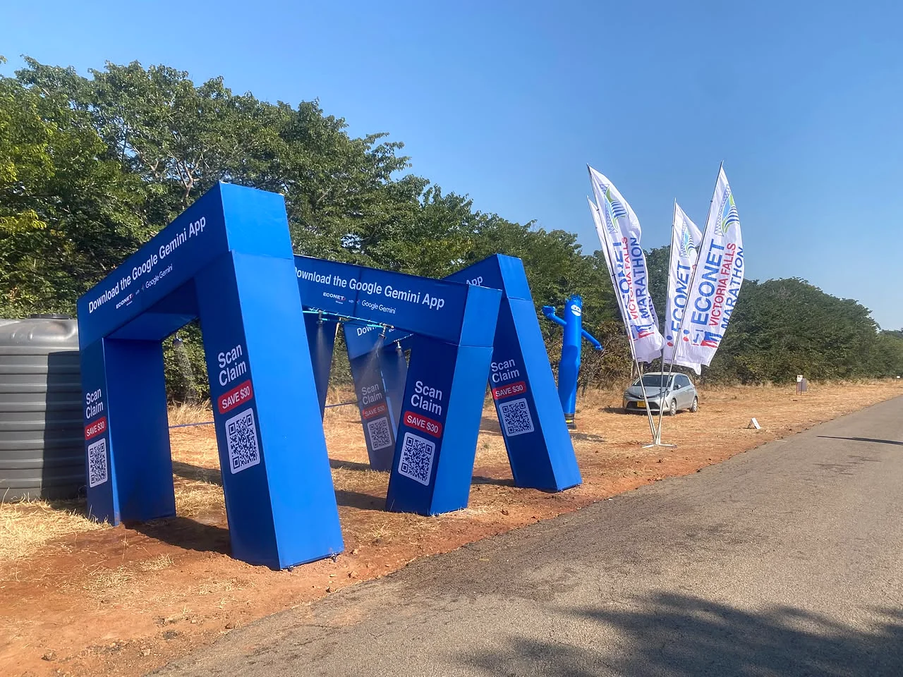Blue Google Gemini promotional arches and Econet Victoria Falls Marathon flags beside a road